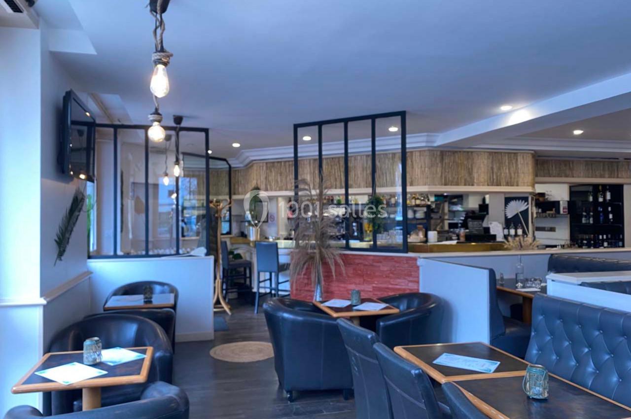 Intérieur d'un café moderne avec fauteuils en cuir, tables en bois et comptoir ouvert sur la cuisine.