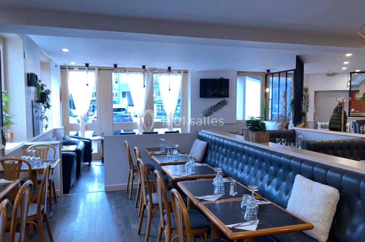 Salle de restaurant lumineuse avec tables en bois, banquettes rembourrées et grandes fenêtres laissant entrer la lumière…