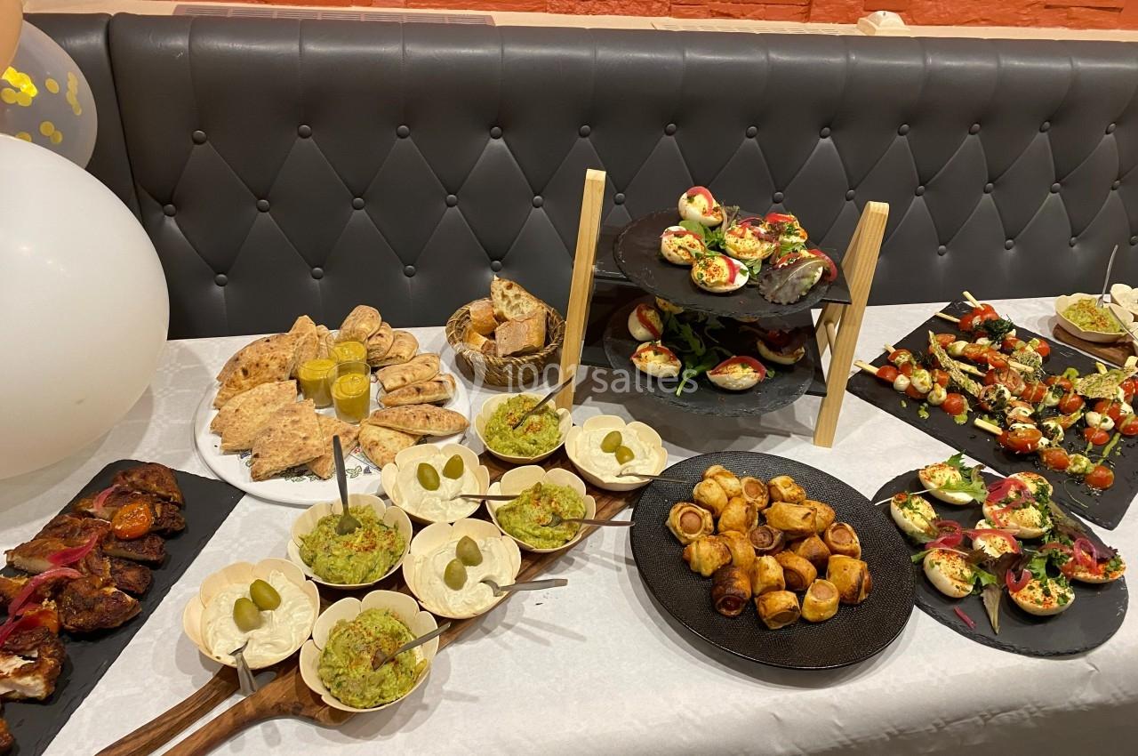 Buffet composé de divers amuse-bouches, pains, verrines et plats salés disposés sur une table blanche.