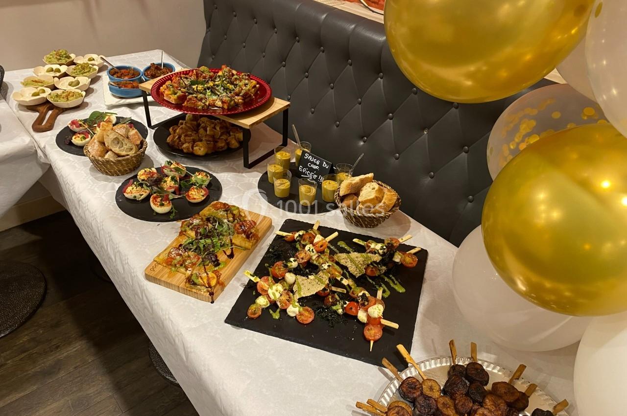 Buffet varié avec plats salés, brochettes, pains et salades, décoré de ballons dorés sur une table blanche.