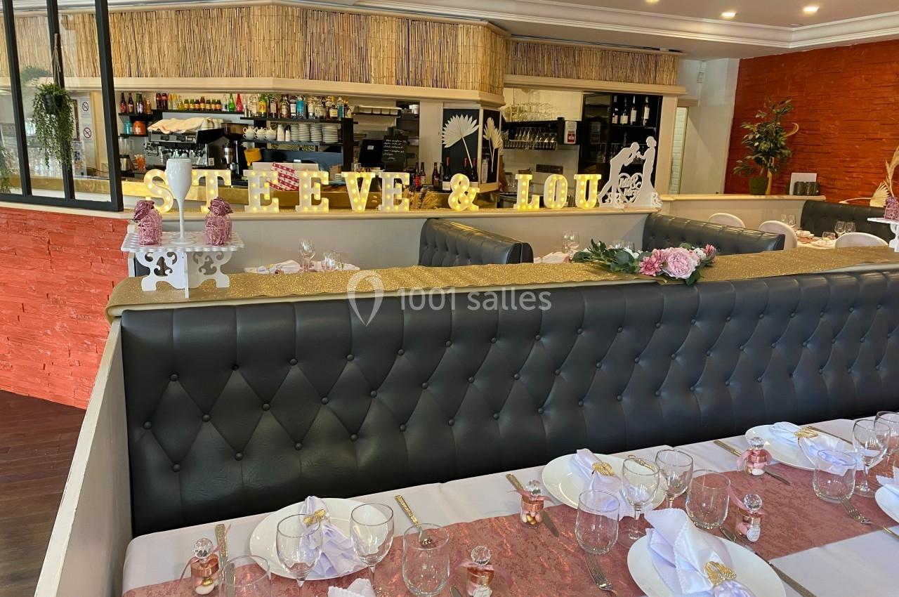 Salle de réception décorée pour un mariage, avec tables dressées, fleurs et une bannière ’Steeve & Lou’.