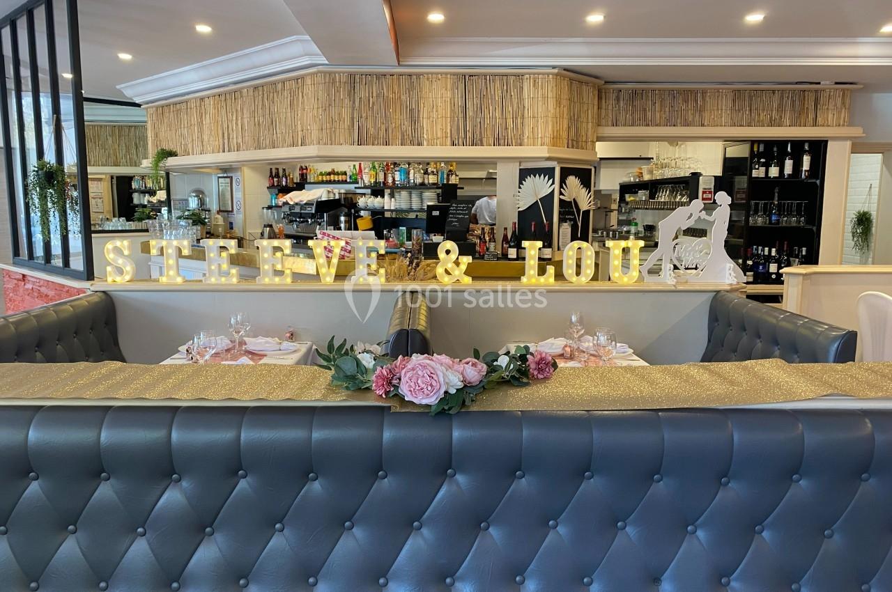 Banquette en cuir gris dans un restaurant décoré pour un mariage avec des fleurs et des lettres lumineuses ’Steve & Lou’.