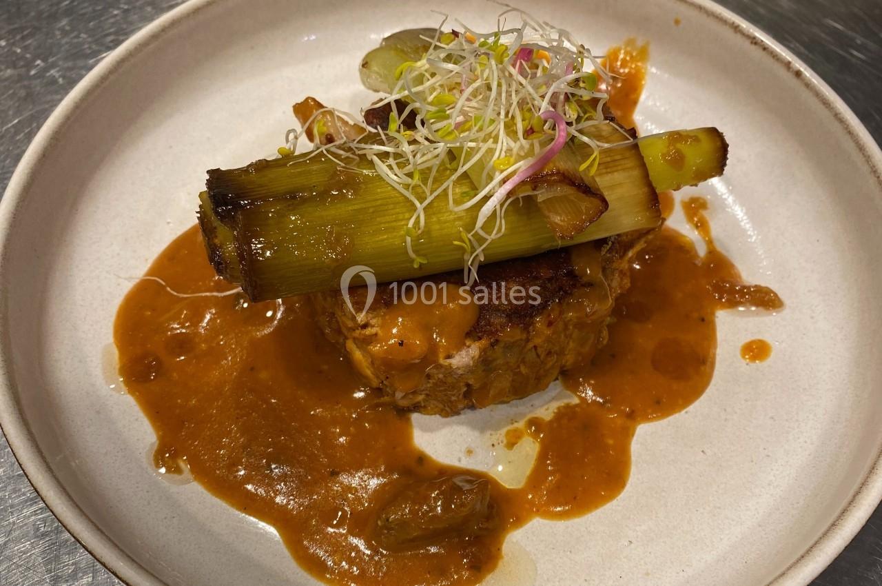 Plat dressé avec un morceau de viande, une sauce brune, un poireau grillé et une garniture de pousses germées.