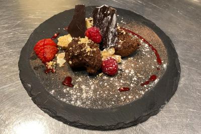 Dessert au chocolat avec framboises fraîches, éclats de biscuit et coulis, présenté sur une assiette en ardoise.