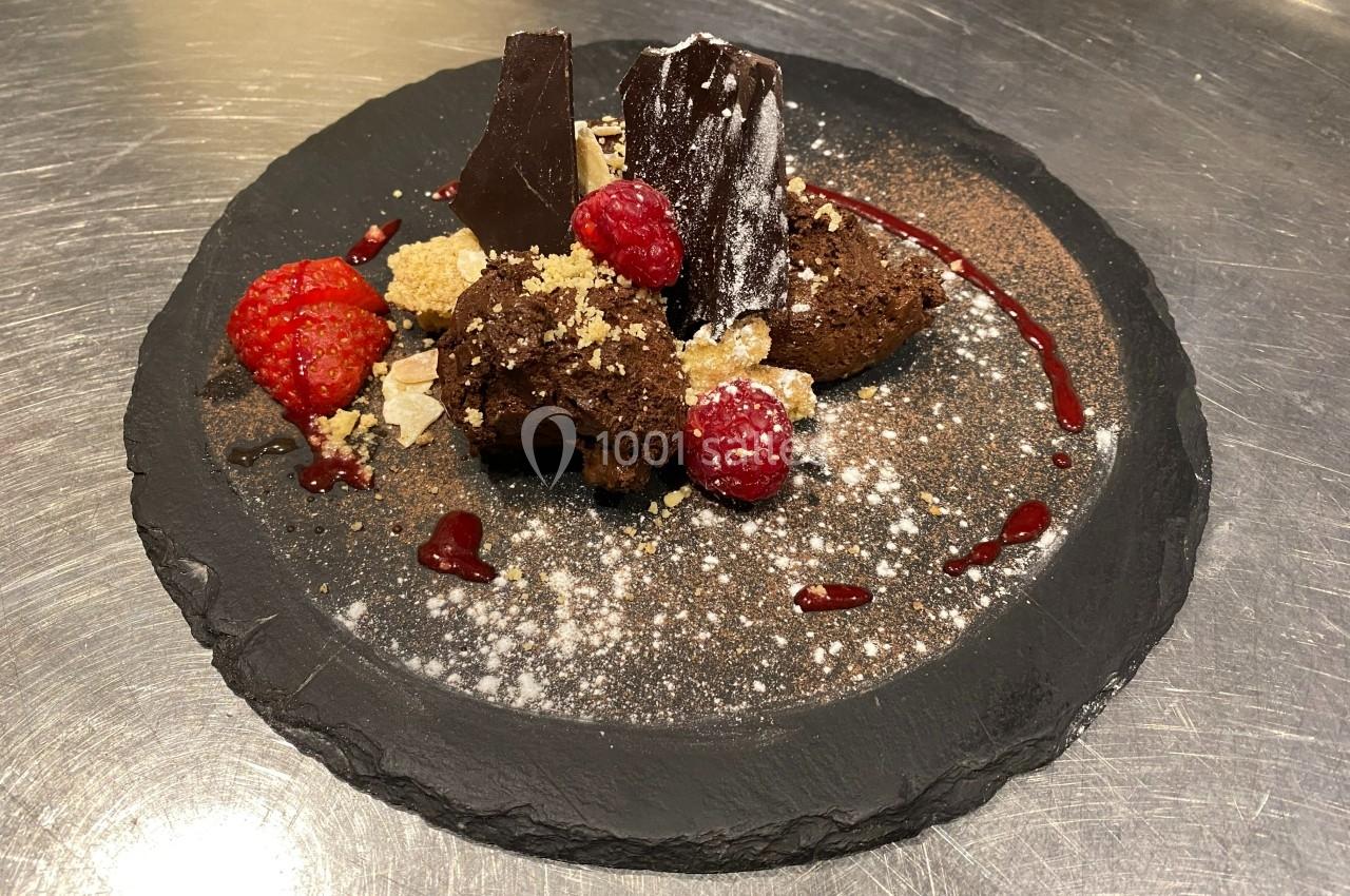 Dessert au chocolat avec framboises fraîches, éclats de biscuit et coulis, présenté sur une assiette en ardoise.