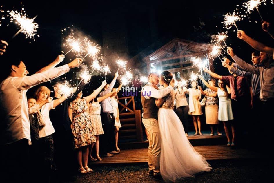 Un couple danse entouré d'invités tenant des cierges magiques allumés dans une ambiance festive en soirée.