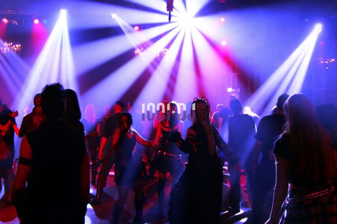 Personnes dansant dans une ambiance festive avec des jeux de lumière colorés dans une salle sombre.