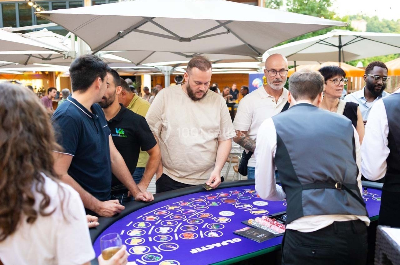 Des personnes jouent autour d'une table de casino en plein air, sous des parasols, dans une ambiance conviviale.