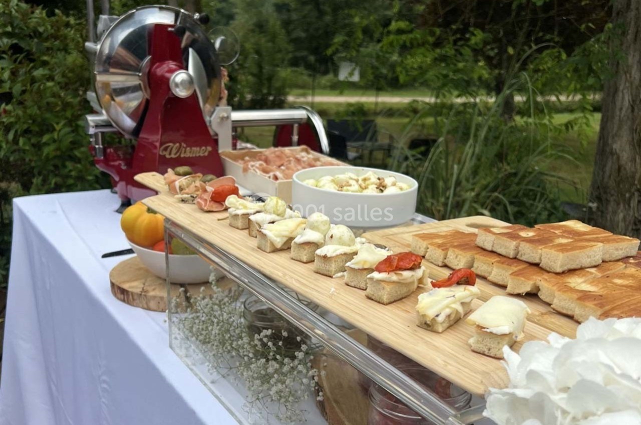 Plateau de dégustation avec bruschettas variées, machine à jambon et décor végétal en arrière-plan.