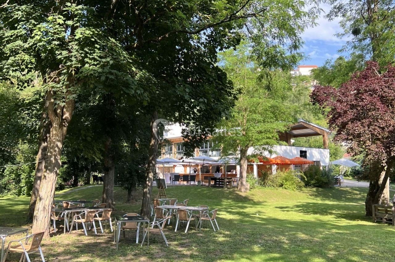 Chaises et tables en métal disposées sur une pelouse ombragée près d'un bâtiment entouré d'arbres.