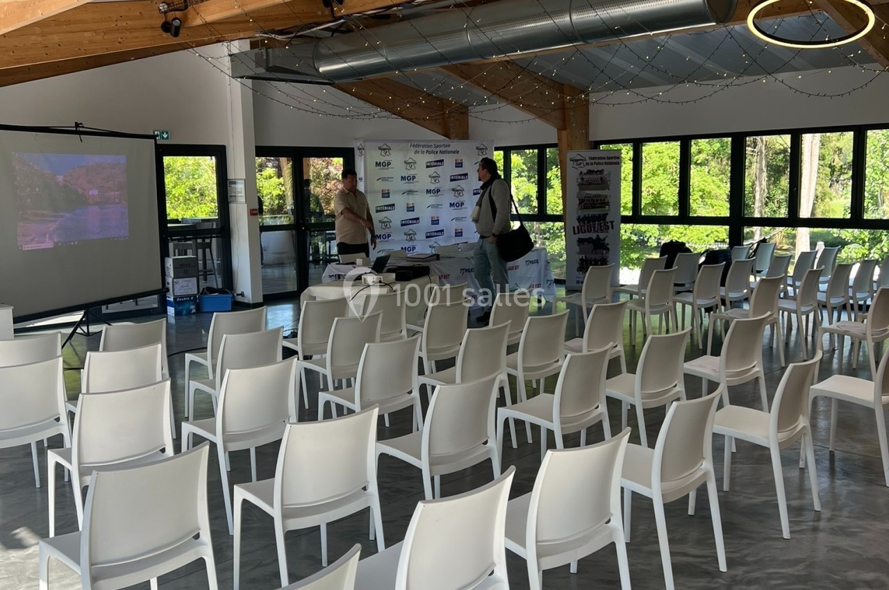 Salle lumineuse avec chaises blanches alignées, écran de projection, structure en bois et grandes baies vitrées donnant sur…