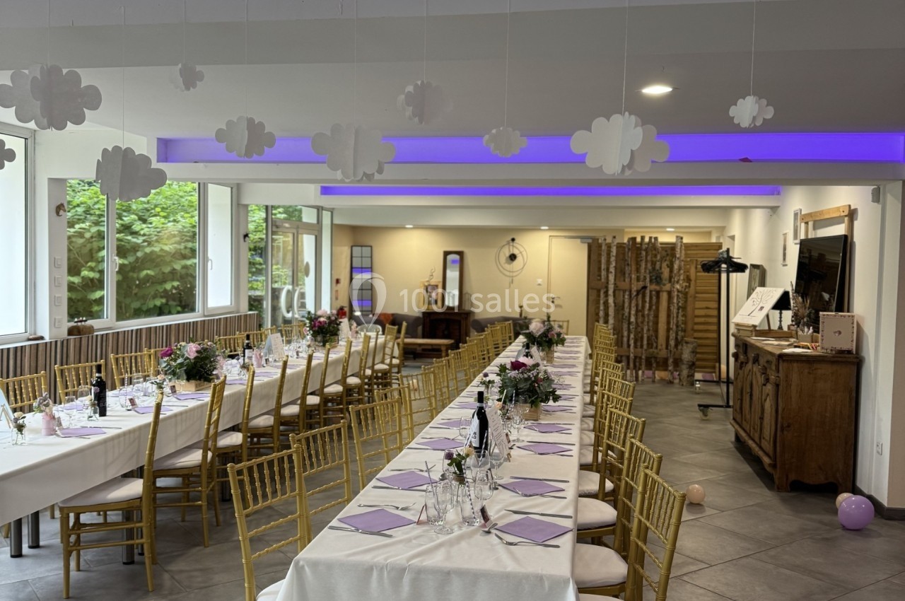 Salle de réception décorée avec de longues tables dressées, des chaises dorées et des nuages suspendus au plafond.
