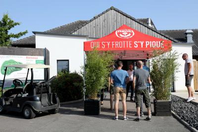 Des personnes rassemblées devant un bâtiment moderne avec des terrasses, des parasols et des voiturettes de golf.