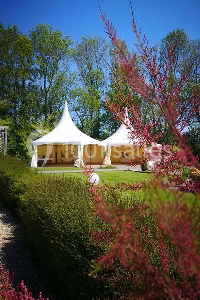 Deux tentes blanches installées sur une pelouse entourée de végétation et d'arbres sous un ciel bleu.