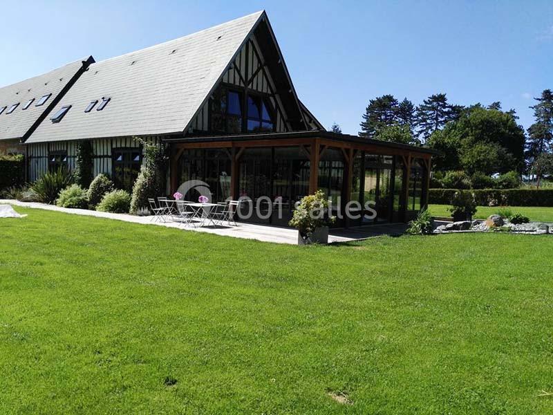 Maison à colombages avec une grande véranda, entourée d'un jardin verdoyant et d'une pelouse bien entretenue.