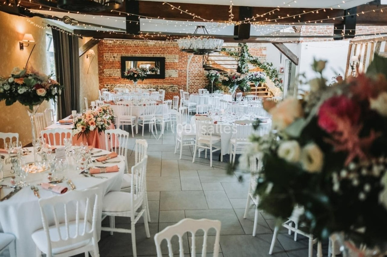 Salle de réception décorée avec des tables rondes, nappes blanches, chaises assorties et arrangements floraux élégants.