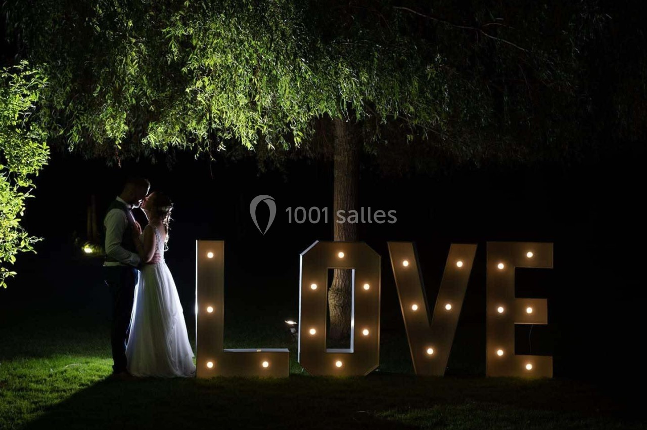 Un couple se tient sous un arbre la nuit, près de grandes lettres lumineuses formant le mot ’LOVE’.