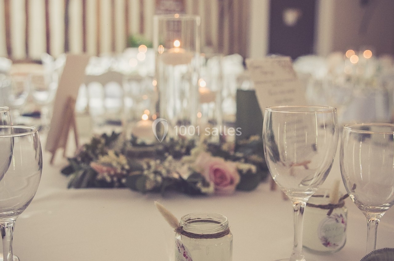 Table décorée pour un événement avec bougies, fleurs et guirlandes lumineuses suspendues en arrière-plan.