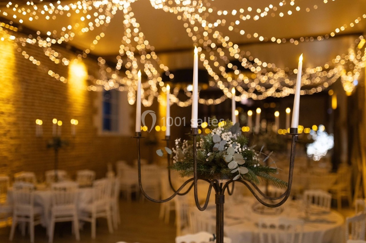 Salle de réception décorée avec des guirlandes lumineuses et un chandelier orné de feuillage et de bougies allumées.