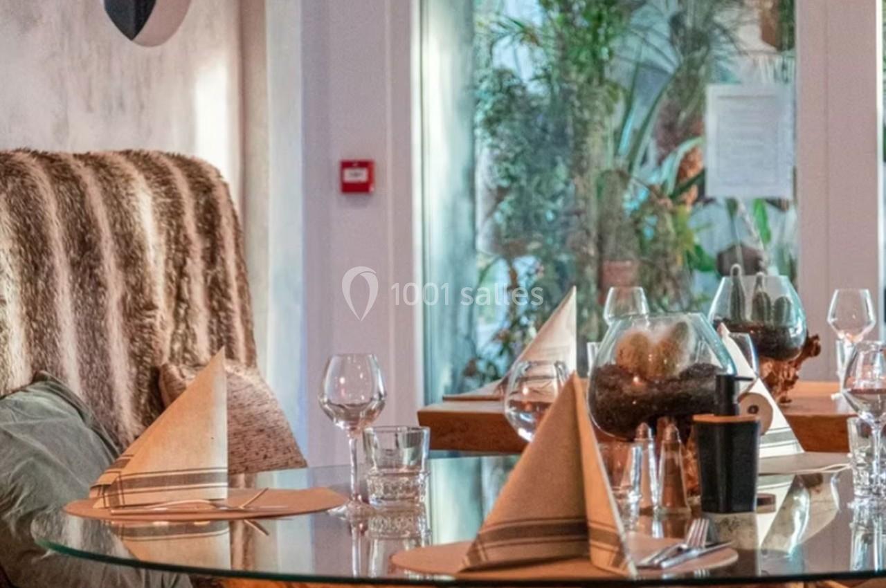 Table dressée avec des serviettes pliées, verres et décoration végétale, dans un restaurant au décor chaleureux.