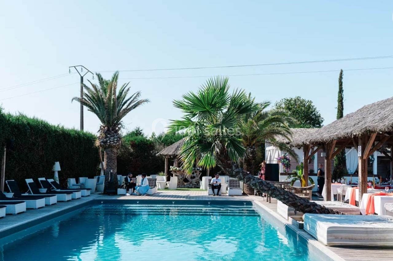 Piscine extérieure entourée de palmiers, transats et espaces de détente sous des toits en chaume.