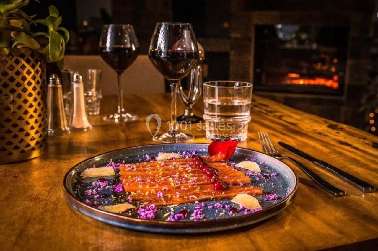 Assiette de saumon fumé décorée de fleurs comestibles et accompagnée de verres de vin rouge sur une table en bois.