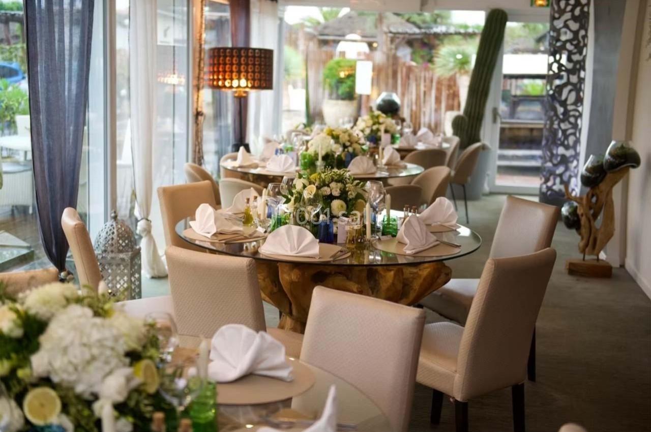 Salle de réception élégante avec tables rondes décorées de fleurs blanches et serviettes pliées, ambiance lumineuse.