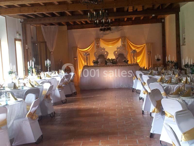 Salle de réception décorée avec des tables dressées, des chaises blanches ornées de nœuds dorés et une table d'honneur…