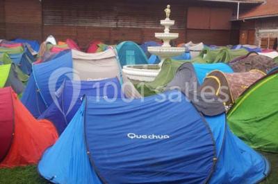 Plusieurs tentes colorées installées sur un terrain herbeux entouré d'arbres.