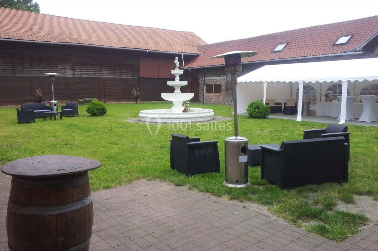 Cour intérieure avec fontaine centrale, mobilier de jardin noir, tonnelle blanche et bâtiments en bois autour.