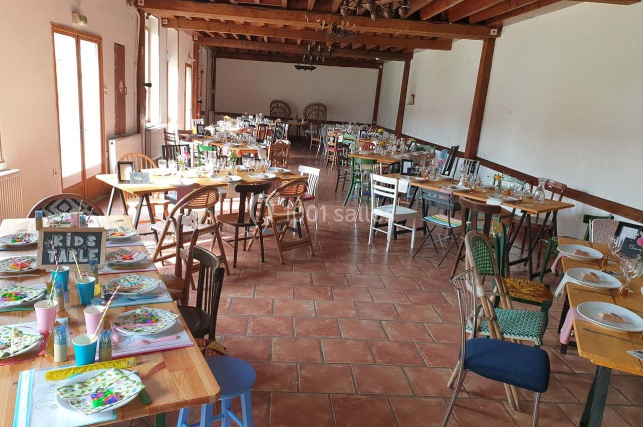 Salle de réception lumineuse avec tables décorées pour un repas, chaises variées et sol en carrelage.