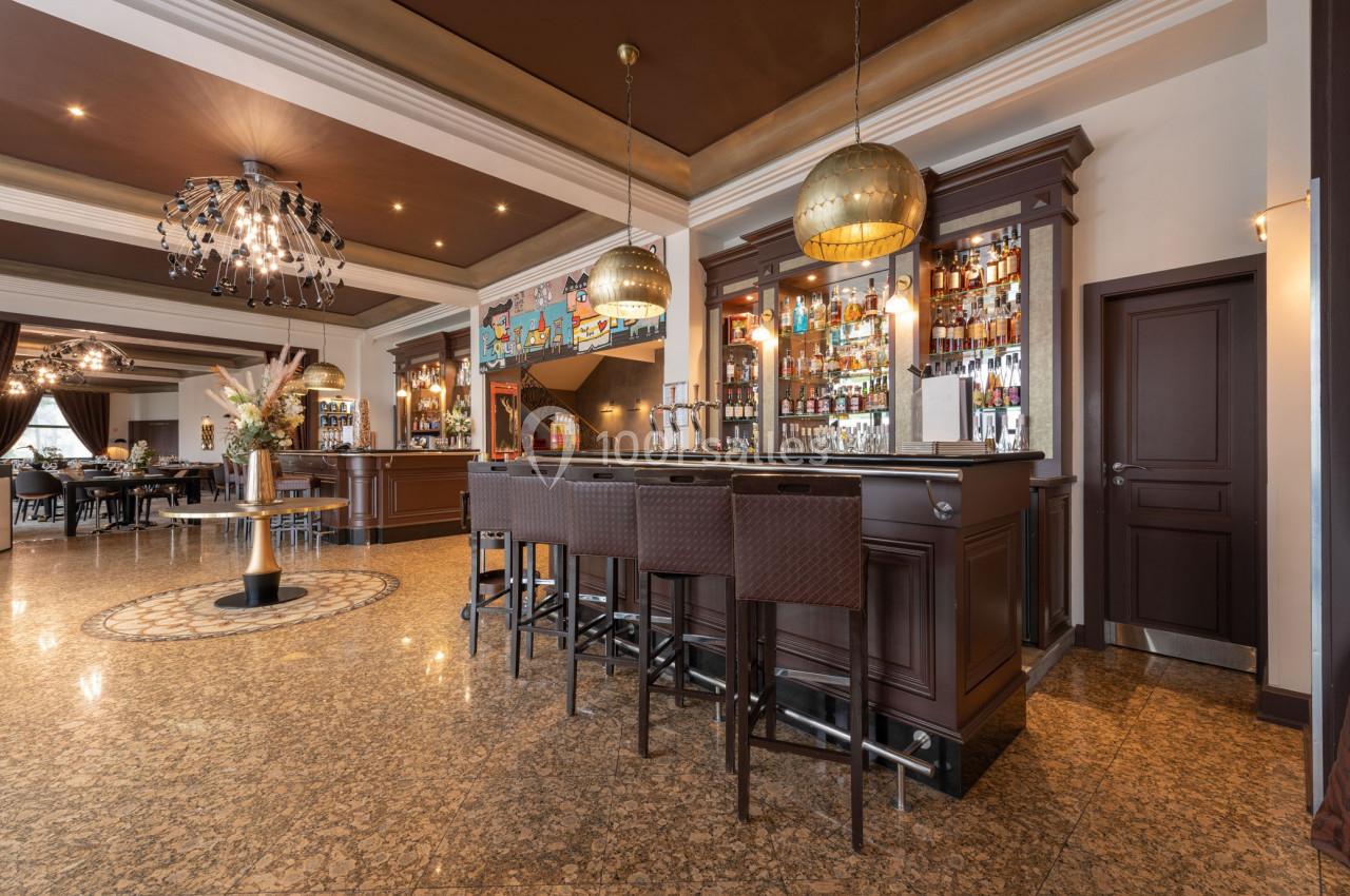 Bar élégant avec comptoir en bois sombre, tabourets hauts, étagères de bouteilles et éclairage décoratif.