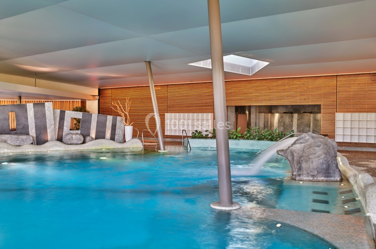 Piscine intérieure avec cascade, entourée de murs en bois et de plantes, éclairée par une lumière naturelle.