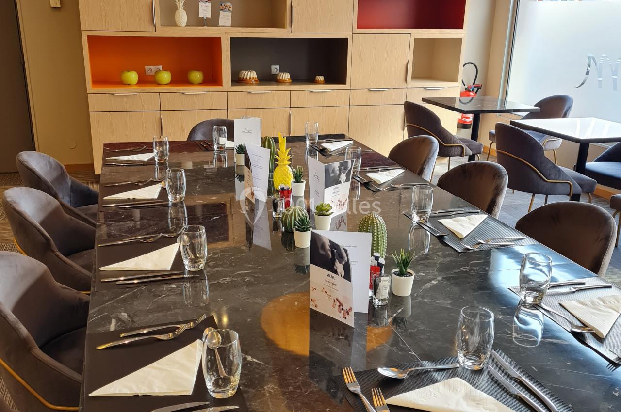 Table dressée avec vaisselle et menus dans une salle de restaurant moderne, éclairée par une grande baie vitrée.