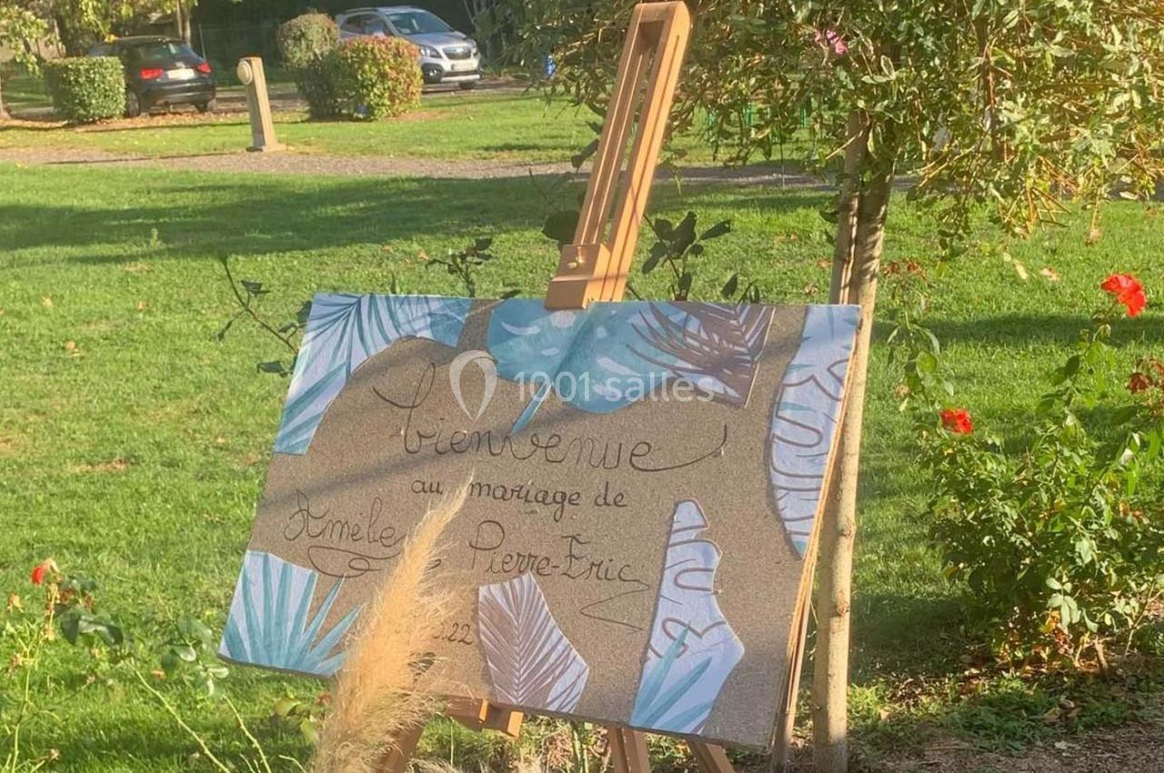 Panneau de bienvenue décoratif pour un mariage, posé sur un chevalet dans un jardin verdoyant.