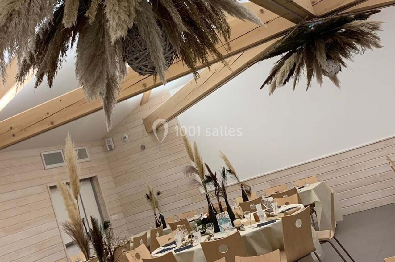 Salle décorée pour un événement avec tables dressées, chaises en bois clair et ornements suspendus en herbes séchées.