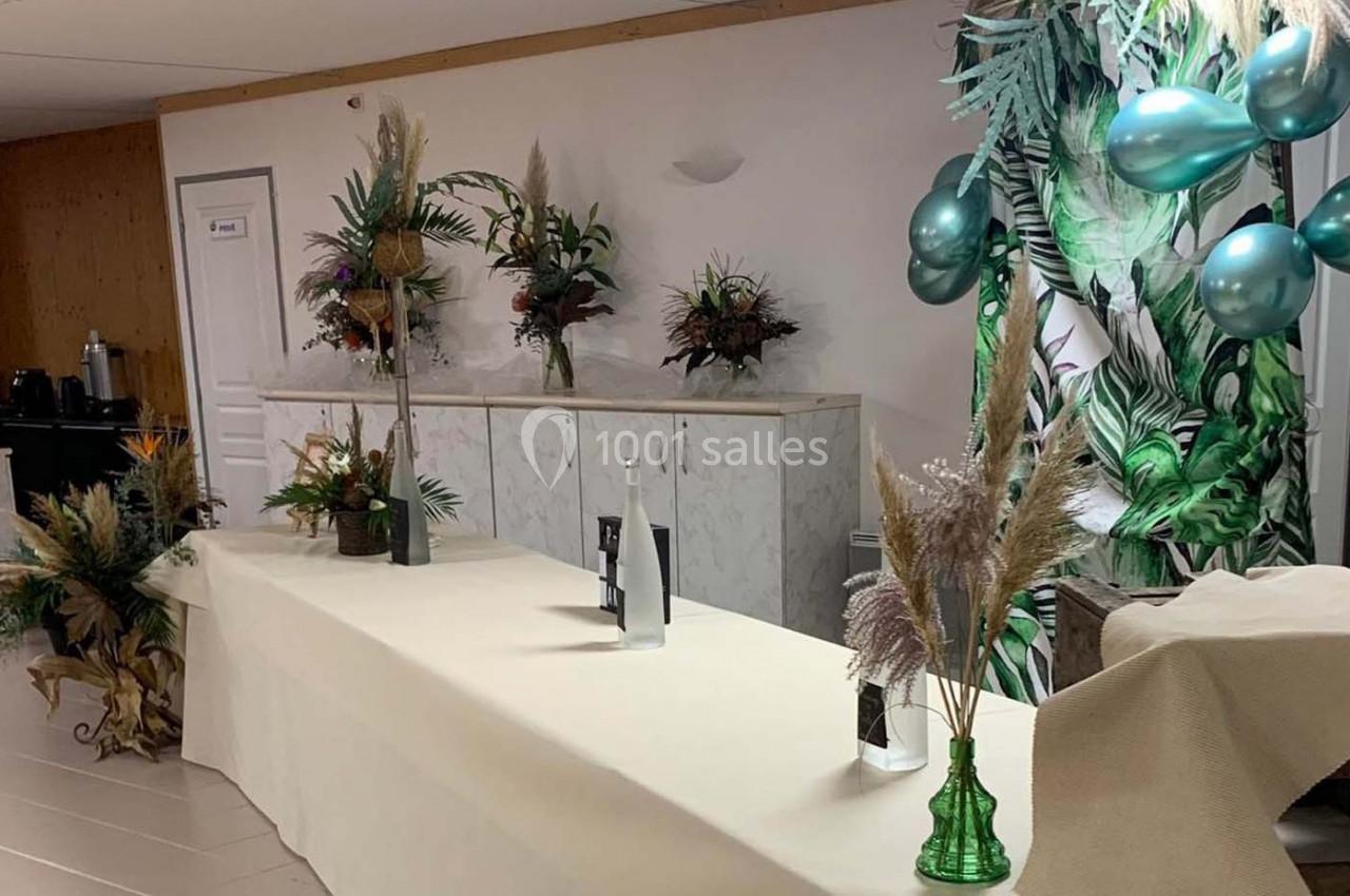 Table décorée avec des plantes, des fleurs séchées et des ballons verts, dans une salle au mur en bois et blanc.