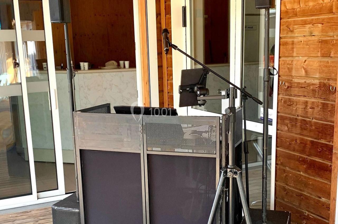 Poste de DJ avec enceintes, micro et tablette installé sur une terrasse en bois devant une porte vitrée.
