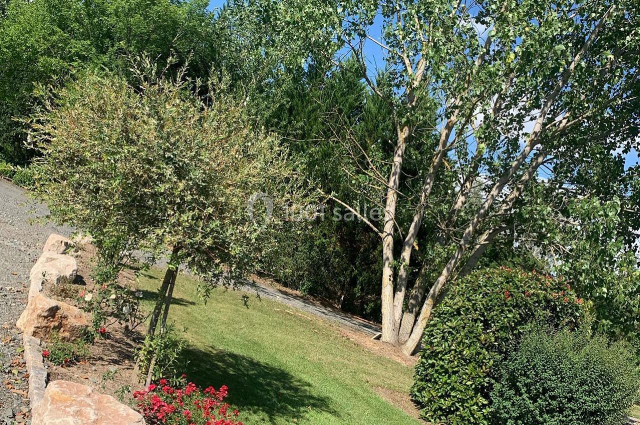 Jardin avec pelouse, arbres, arbustes et fleurs rouges, bordé par une allée en gravier et un muret en pierre.