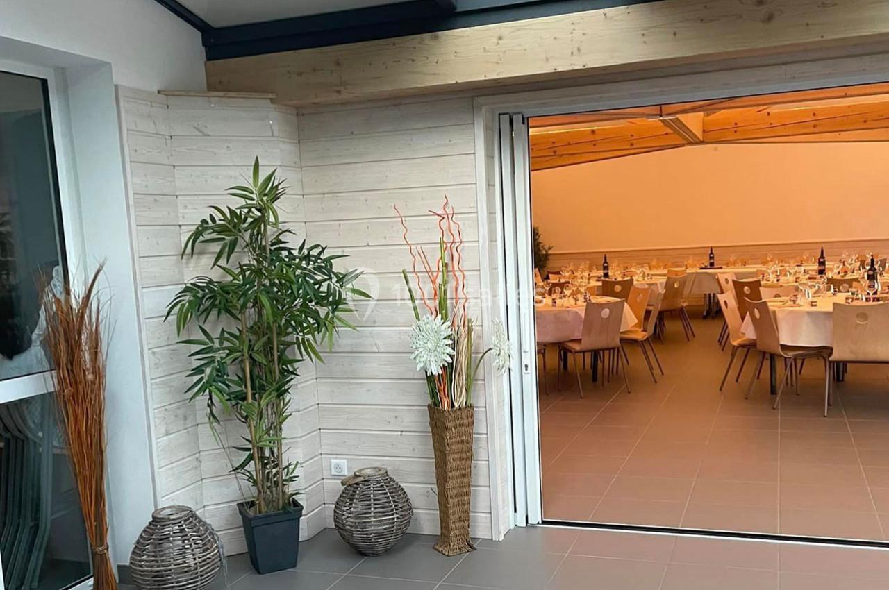 Vue d'une salle de réception lumineuse avec tables dressées, accessible depuis une terrasse décorée de plantes et paniers.