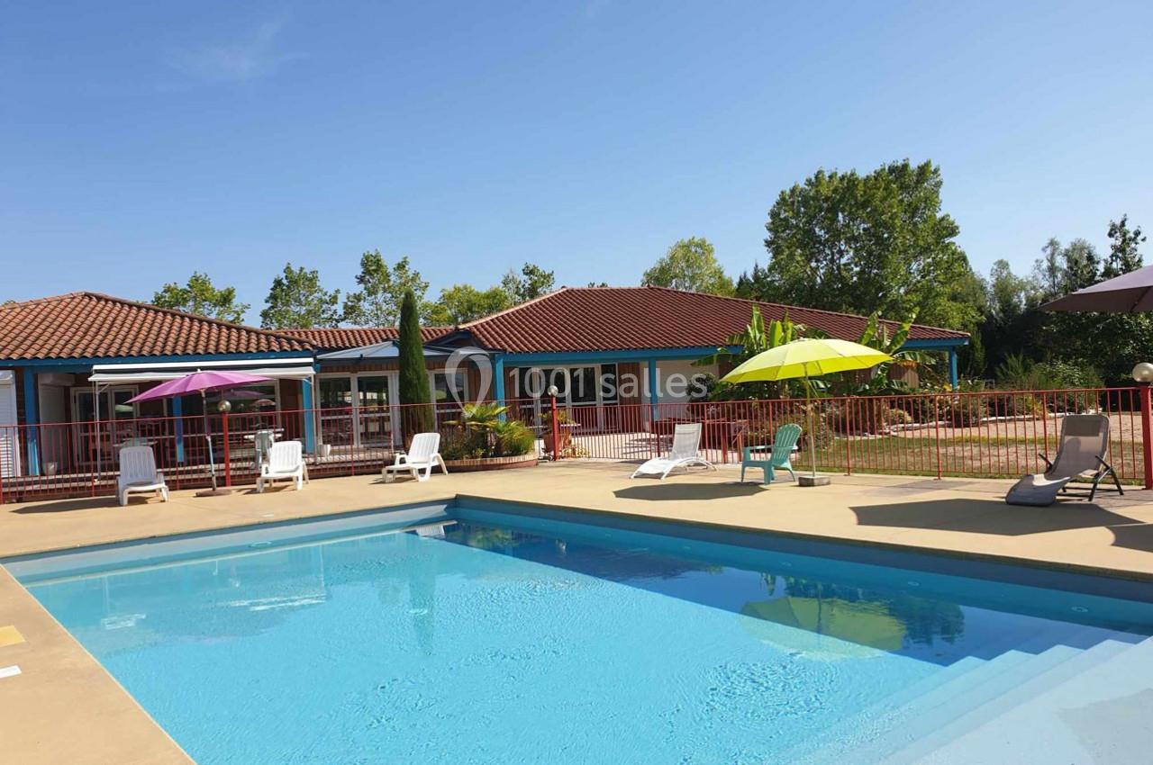 Piscine extérieure entourée de transats et parasols colorés, avec un bâtiment à toit rouge en arrière-plan.