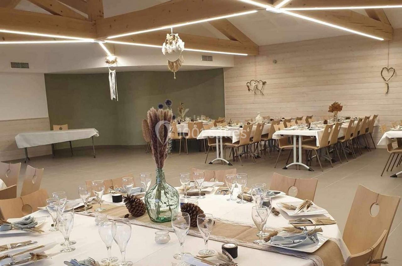 Salle de réception décorée avec des tables dressées, des éléments naturels et un éclairage moderne en bois.