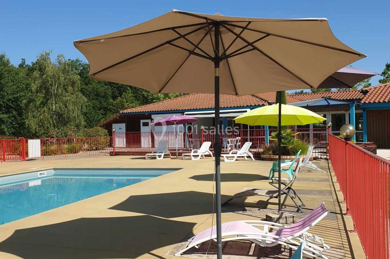 Piscine extérieure entourée de transats colorés et de parasols, avec des bâtiments en arrière-plan.