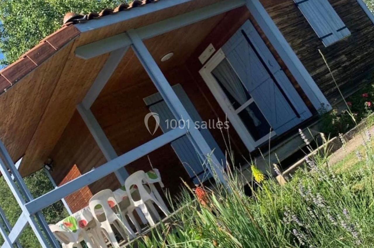 Chalet en bois avec terrasse couverte, mobilier de jardin blanc et entouré de végétation.