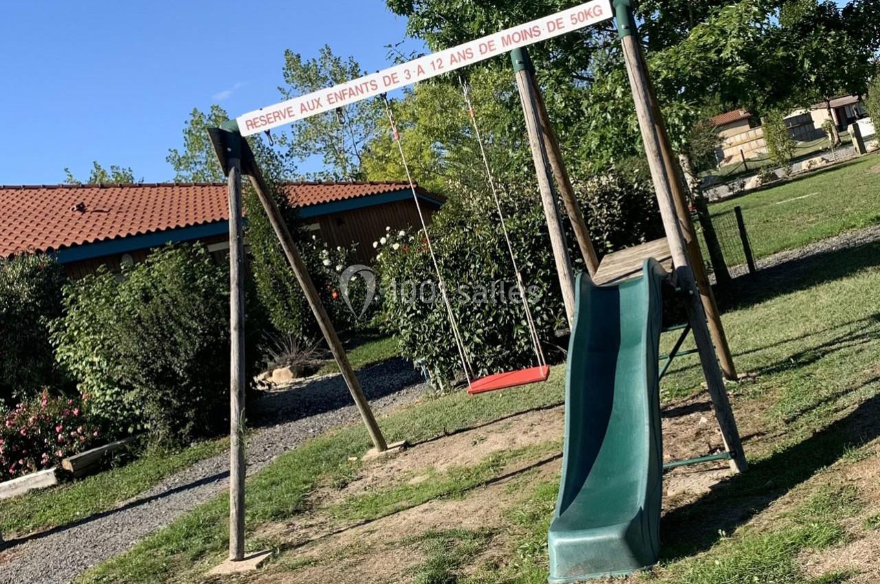 Structure de jeu extérieure avec balançoire et toboggan, réservée aux enfants de 3 à 12 ans, dans un espace vert.