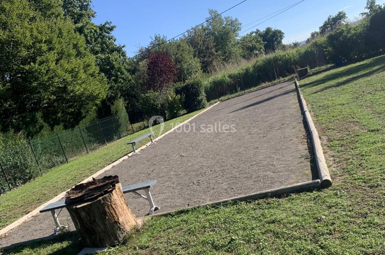 Terrain de pétanque en plein air entouré de verdure, avec des bancs et une souche d'arbre au premier plan.