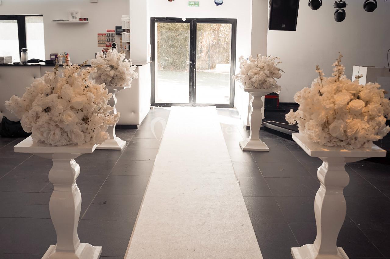 Allée centrale décorée de colonnes blanches ornées de bouquets de fleurs blanches dans une salle lumineuse.
