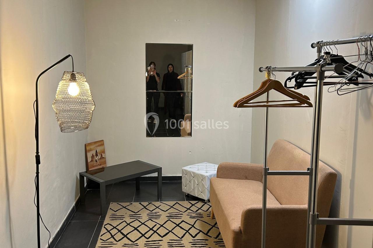 Salle minimaliste avec canapé beige, miroir, portants à vêtements, tapis géométrique et lampe suspendue.