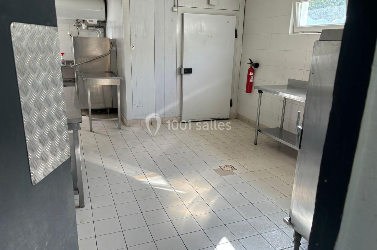 Cuisine professionnelle vide avec équipements en inox, sol carrelé, porte froide et extincteur fixé au mur.