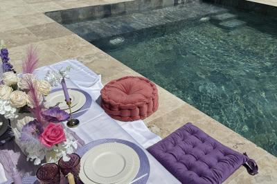 Table dressée avec vaisselle et fleurs bleues près d'une piscine entourée de dalles claires et de végétation.